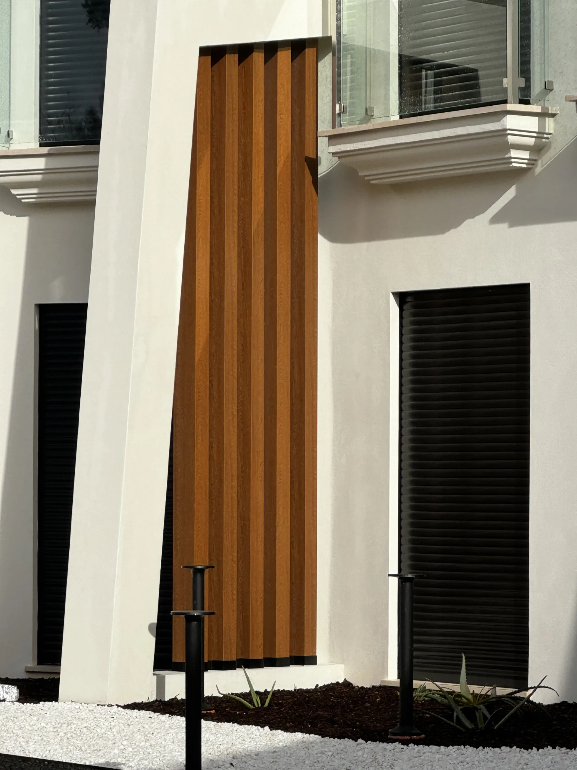 Detalhe de painel decorativo em réguas verticais tom madeira, junto a varandas envidraçadas
